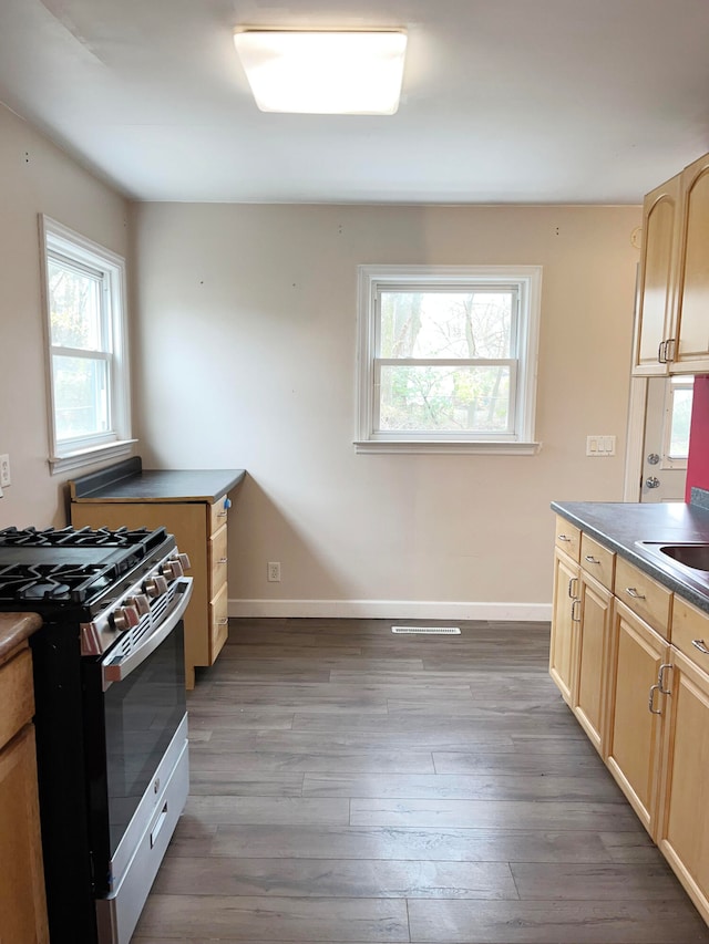 kitchen with stainless steel range with gas cooktop, dark countertops, light brown cabinets, wood finished floors, and baseboards