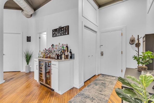 foyer entrance with light hardwood / wood-style floors, a high ceiling, wine cooler, and bar area