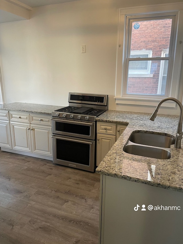 kitchen featuring hardwood / wood-style floors, light stone countertops, white cabinetry, sink, and range with two ovens