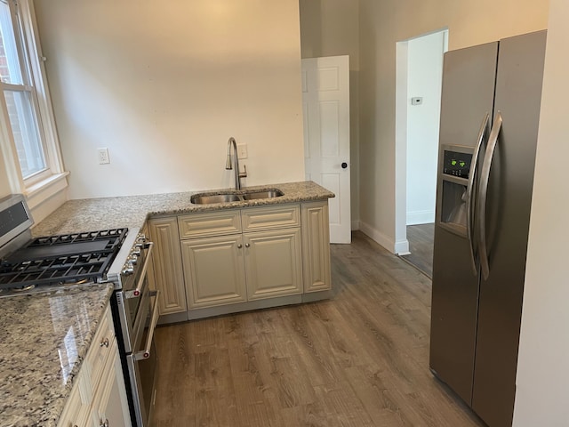 kitchen with kitchen peninsula, appliances with stainless steel finishes, sink, dark wood-type flooring, and light stone countertops