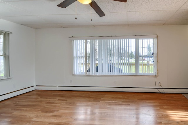 unfurnished room with light wood-type flooring, baseboard heating, and a wealth of natural light