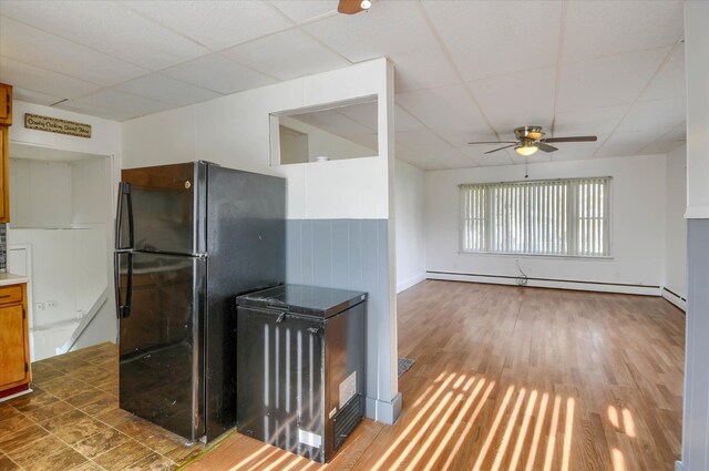 kitchen featuring black refrigerator, a drop ceiling, ceiling fan, a baseboard heating unit, and dark hardwood / wood-style floors