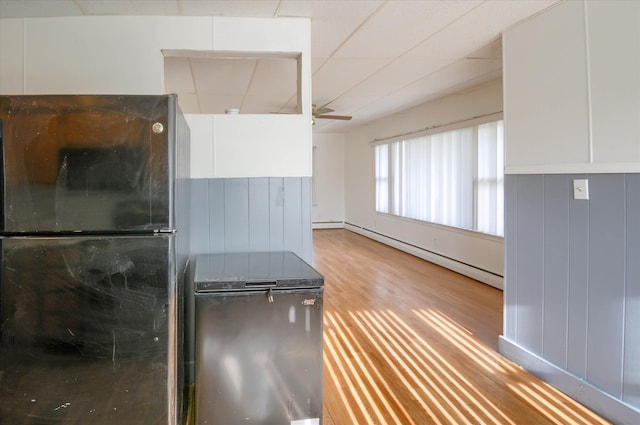 kitchen featuring ceiling fan, light hardwood / wood-style flooring, a baseboard heating unit, black refrigerator, and white cabinets