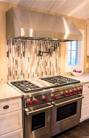 kitchen featuring light stone countertops, tasteful backsplash, wall chimney exhaust hood, range with two ovens, and white cabinets