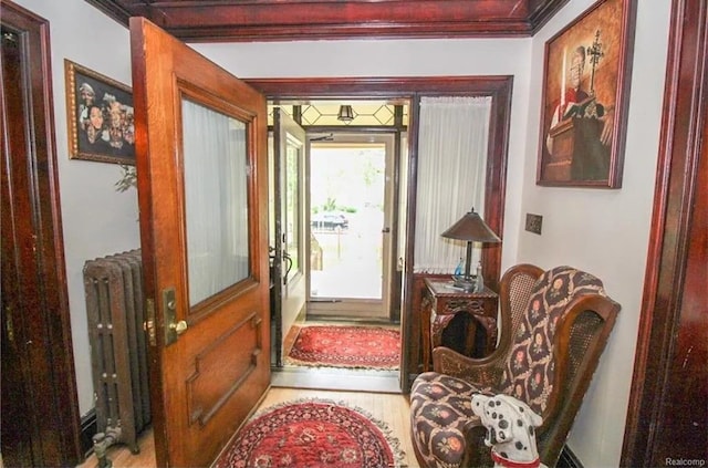 doorway to outside with radiator heating unit, light wood-type flooring, and ornamental molding