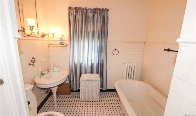 bathroom featuring a washtub, toilet, radiator heating unit, and tile walls