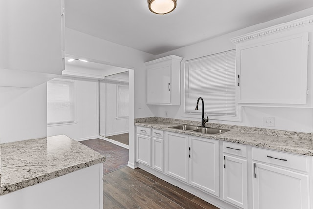 kitchen with white cabinets, sink, light stone countertops, and dark wood-type flooring