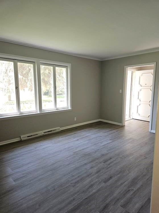 unfurnished room featuring baseboard heating, crown molding, and dark hardwood / wood-style floors