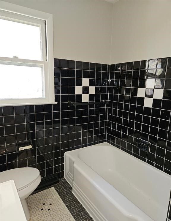 bathroom featuring tile patterned flooring, a bathtub, toilet, and tile walls