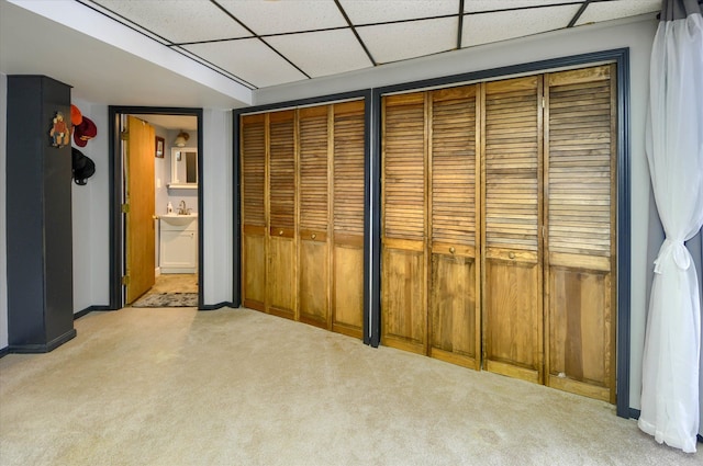 unfurnished bedroom with a paneled ceiling, multiple closets, sink, and light colored carpet