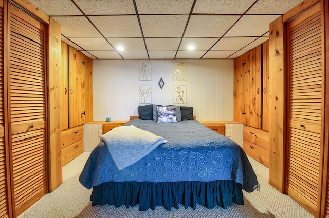 carpeted bedroom featuring a drop ceiling and wood walls