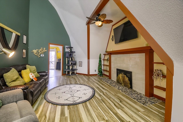 living room with a towering ceiling, a textured ceiling, ceiling fan, light hardwood / wood-style floors, and a tiled fireplace