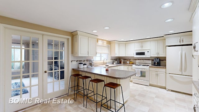 kitchen with kitchen peninsula, a kitchen breakfast bar, french doors, white appliances, and sink