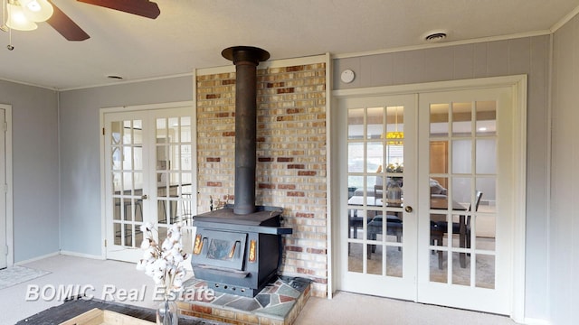 living room with carpet, a wood stove, french doors, crown molding, and ceiling fan