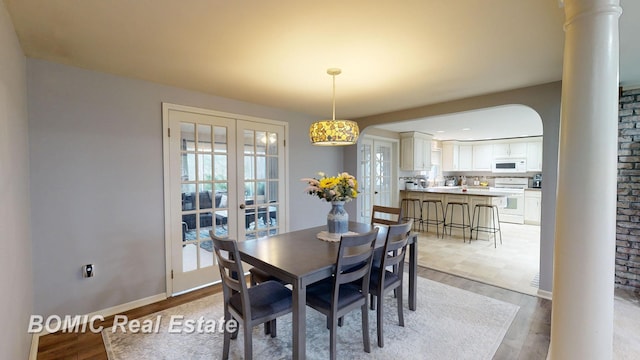 dining space featuring french doors, light wood-type flooring, and decorative columns