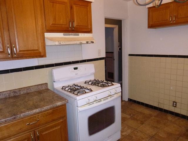 kitchen featuring gas range gas stove, dark tile patterned flooring, and tile walls