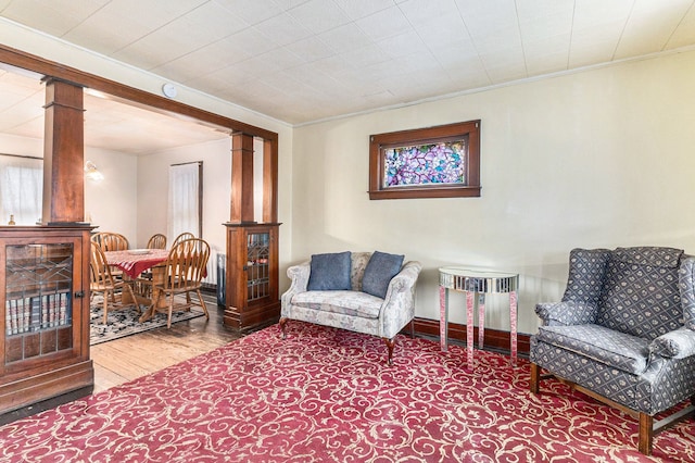 living area with decorative columns, crown molding, and wood finished floors