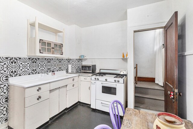 kitchen with white gas range, light countertops, white cabinetry, a sink, and stainless steel microwave