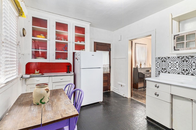 kitchen featuring freestanding refrigerator, white cabinetry, light countertops, glass insert cabinets, and decorative backsplash