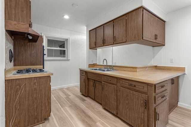 kitchen featuring gas stovetop, sink, ornamental molding, and light wood-type flooring