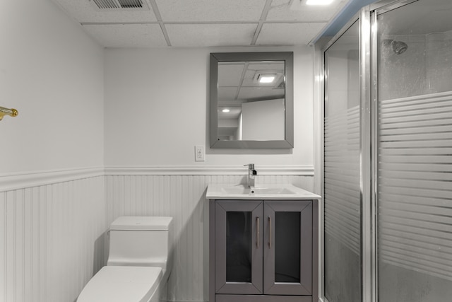 bathroom featuring a paneled ceiling, vanity, wooden walls, toilet, and a shower with shower door