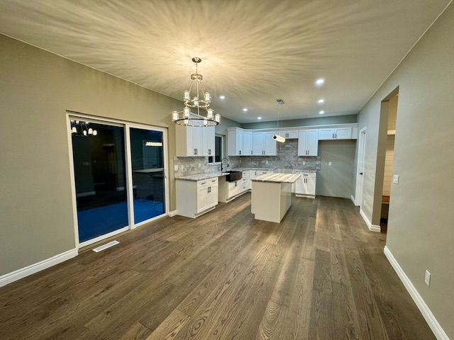 kitchen with decorative backsplash, dark wood-type flooring, white cabinets, a center island, and hanging light fixtures