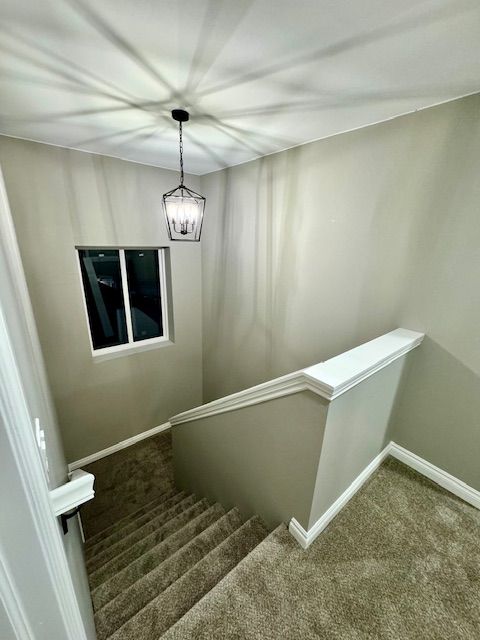 stairs with carpet floors and an inviting chandelier