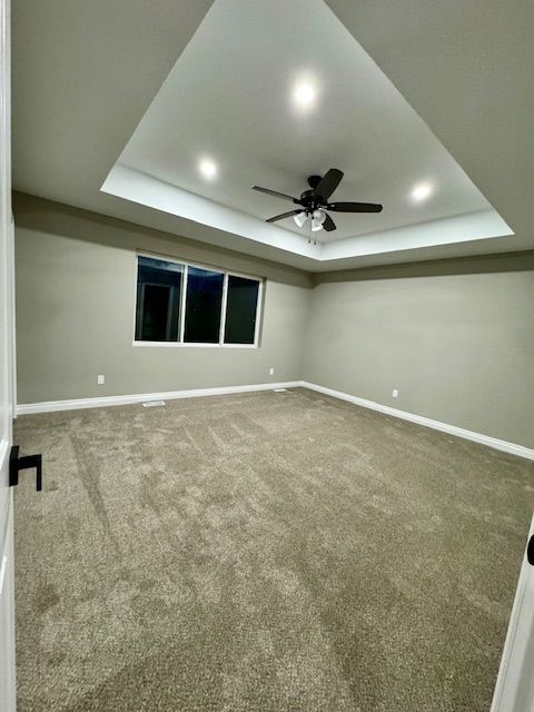 empty room with a raised ceiling, ceiling fan, and carpet