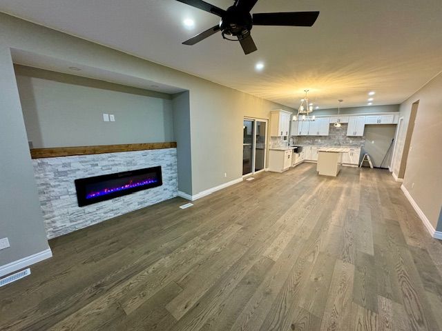 unfurnished living room featuring hardwood / wood-style floors, ceiling fan with notable chandelier, and a fireplace