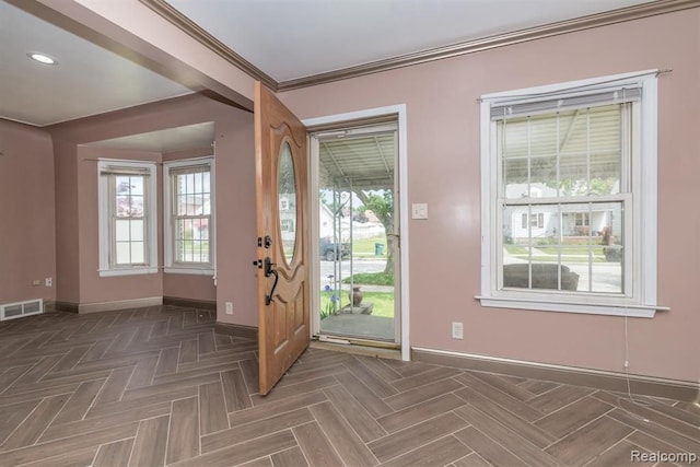 foyer with dark parquet flooring, crown molding, and plenty of natural light