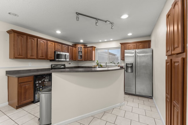 kitchen featuring track lighting, a textured ceiling, stainless steel appliances, beverage cooler, and a center island