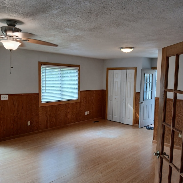 spare room with a textured ceiling, light hardwood / wood-style flooring, ceiling fan, and wooden walls