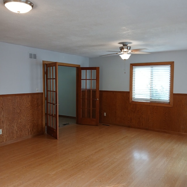 unfurnished room featuring french doors, light hardwood / wood-style flooring, and wood walls