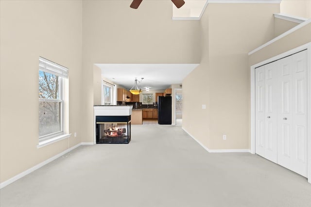 unfurnished living room with a multi sided fireplace, ceiling fan, a towering ceiling, and light colored carpet