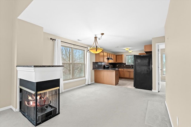 kitchen with hanging light fixtures, a multi sided fireplace, tasteful backsplash, light colored carpet, and black appliances