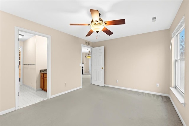 unfurnished bedroom featuring connected bathroom, multiple windows, ceiling fan, and light colored carpet