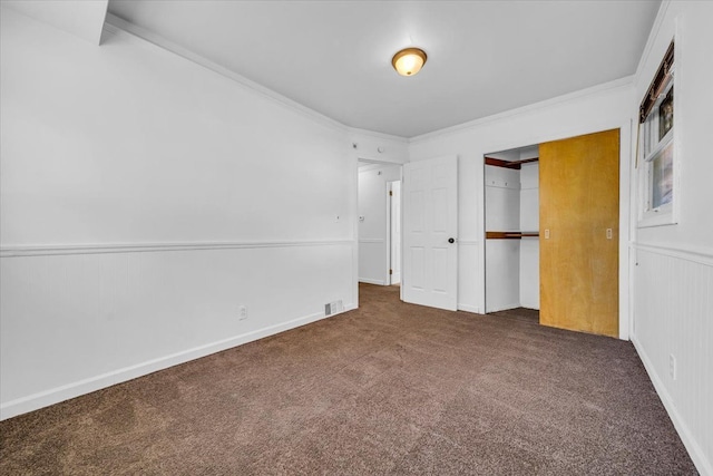 unfurnished bedroom featuring wooden walls, dark carpet, a closet, and crown molding