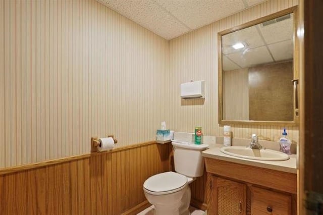 bathroom with wood walls, a drop ceiling, vanity, and toilet