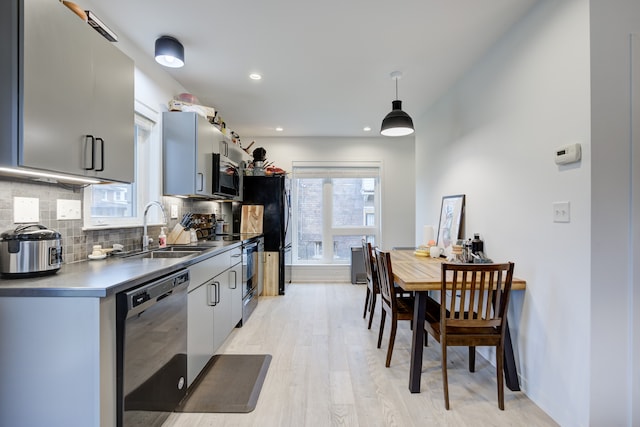 kitchen featuring sink, tasteful backsplash, decorative light fixtures, appliances with stainless steel finishes, and light wood-type flooring