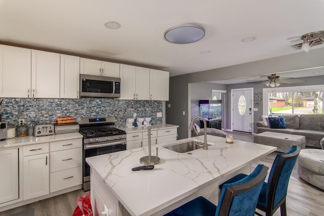 kitchen with light stone countertops, appliances with stainless steel finishes, a kitchen island with sink, white cabinets, and light hardwood / wood-style floors