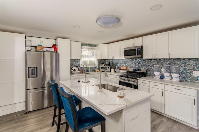 kitchen with appliances with stainless steel finishes, sink, light hardwood / wood-style floors, white cabinetry, and an island with sink