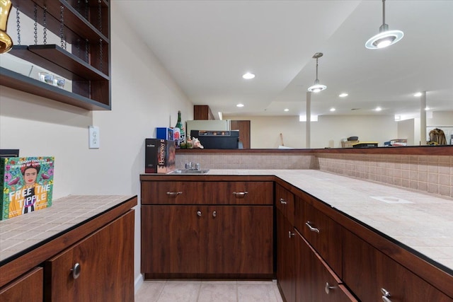 kitchen featuring dark brown cabinets, tile counters, hanging light fixtures, and light tile patterned flooring