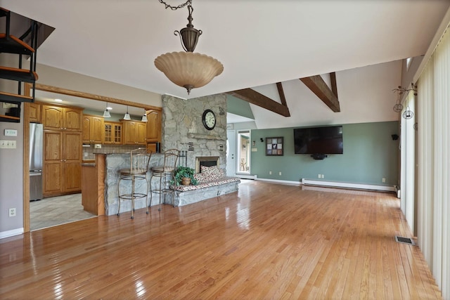 unfurnished living room featuring vaulted ceiling with beams, a stone fireplace, light hardwood / wood-style flooring, and a baseboard radiator