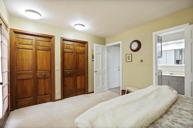 bedroom featuring light carpet, connected bathroom, and multiple closets