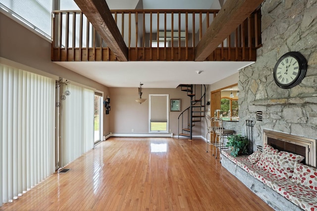 unfurnished living room with hardwood / wood-style floors, a stone fireplace, a high ceiling, and a baseboard heating unit