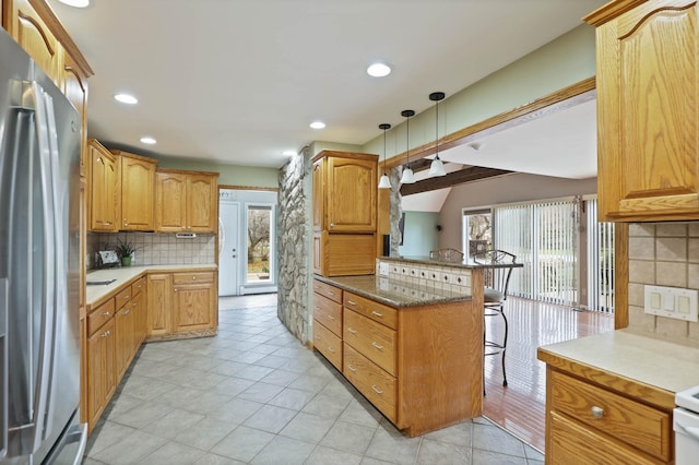 kitchen featuring kitchen peninsula, a kitchen breakfast bar, a wealth of natural light, decorative light fixtures, and stainless steel refrigerator