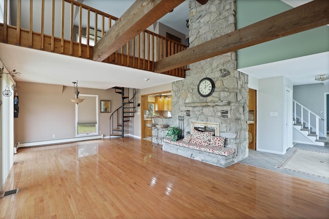 unfurnished living room with a high ceiling, light hardwood / wood-style floors, a stone fireplace, and a baseboard heating unit