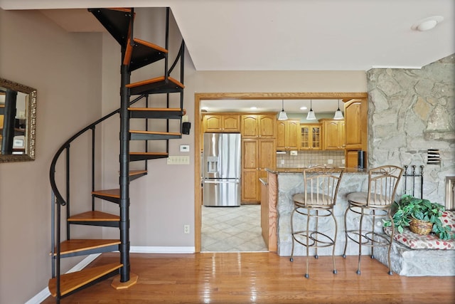 kitchen featuring kitchen peninsula, stainless steel refrigerator with ice dispenser, light wood-type flooring, decorative backsplash, and light stone counters