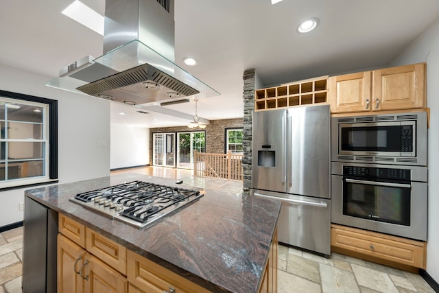 kitchen with a center island, light brown cabinets, dark stone counters, island range hood, and appliances with stainless steel finishes