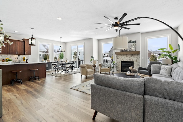 living room with a ceiling fan, a glass covered fireplace, a textured ceiling, light wood-type flooring, and recessed lighting